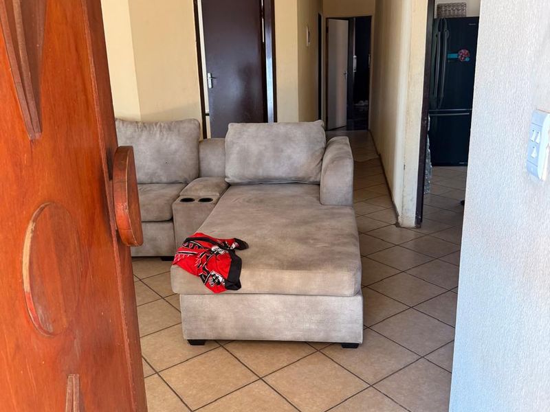A living area featuring tiled flooring and a textured ceiling, leading into a hallway with access to additional rooms.