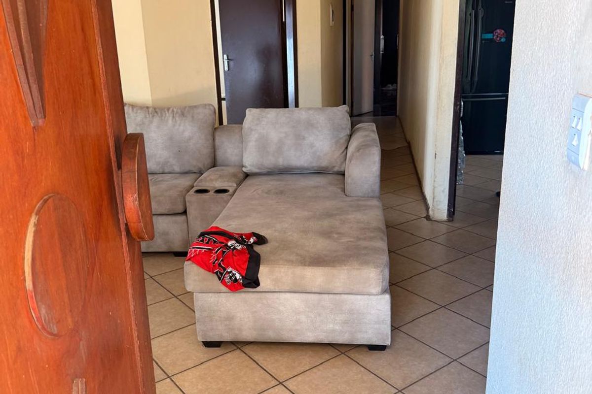 A living area featuring tiled flooring and a textured ceiling, leading into a hallway with access to additional rooms.
