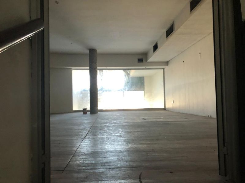 An empty, open-plan retail space featuring a structural column, large window, and integrated ceiling air conditioning vents, ready for custom fit-out.