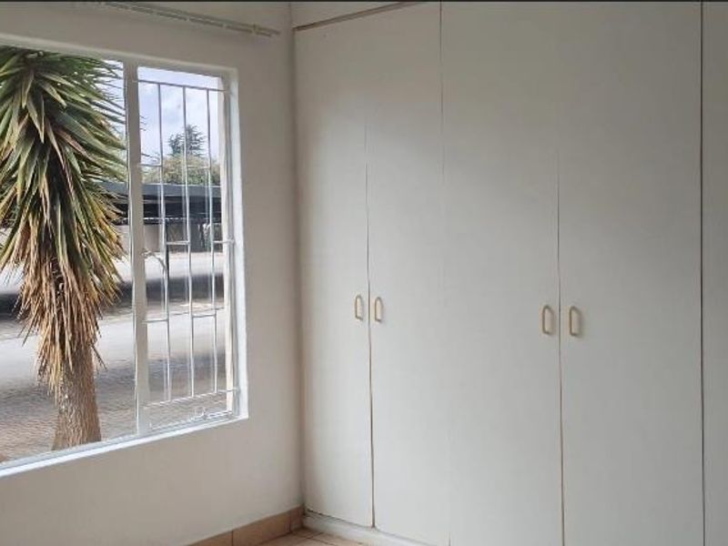 A bright, empty bedroom featuring extensive built-in cupboards and a large window with security bars, offering a clean and functional space.