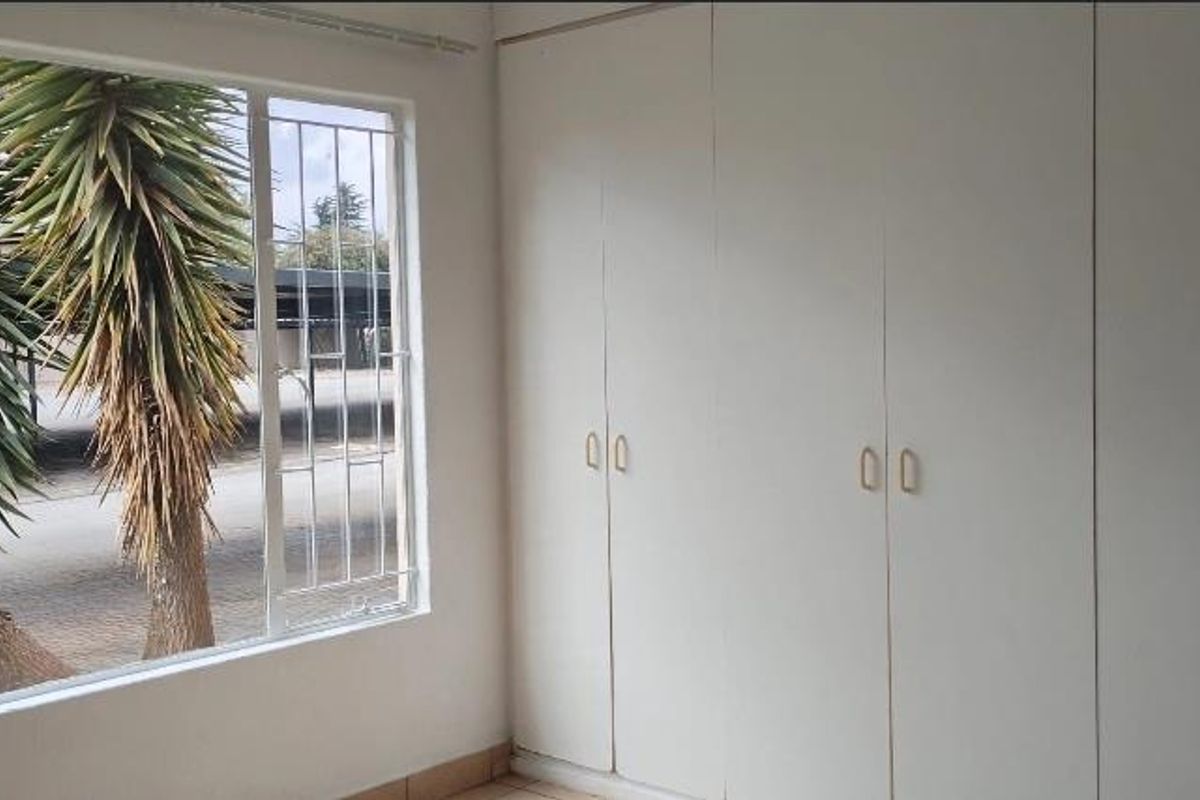 A bright, empty bedroom featuring extensive built-in cupboards and a large window with security bars, offering a clean and functional space.