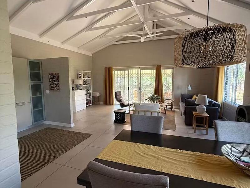Spacious open-plan living and dining area featuring a high vaulted ceiling with exposed trusses, tiled floors, and large sliding doors leading to the outdoors.