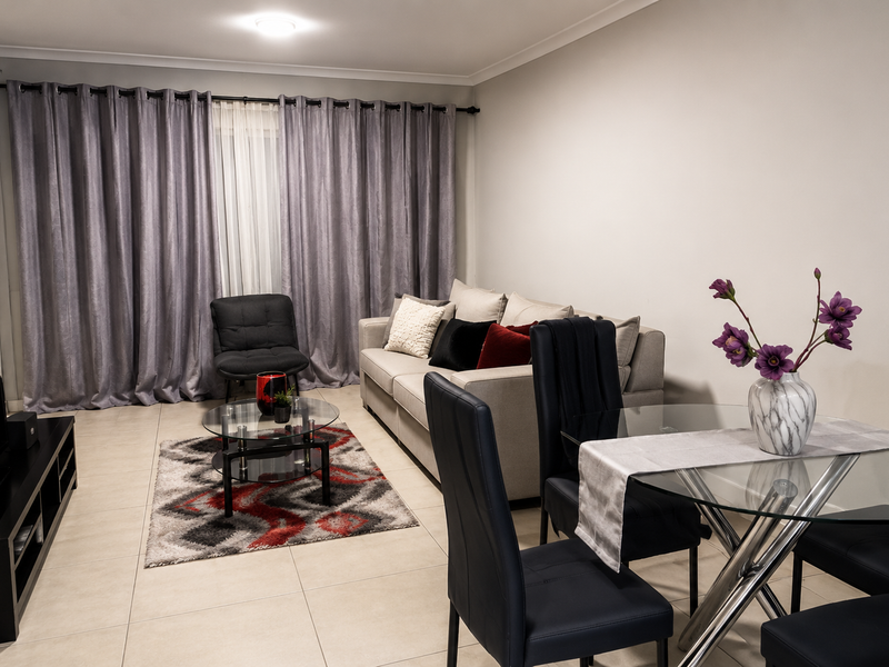 An open-plan living and dining area featuring neutral tiled flooring and full-length window treatments, creating a functional and well-lit space.