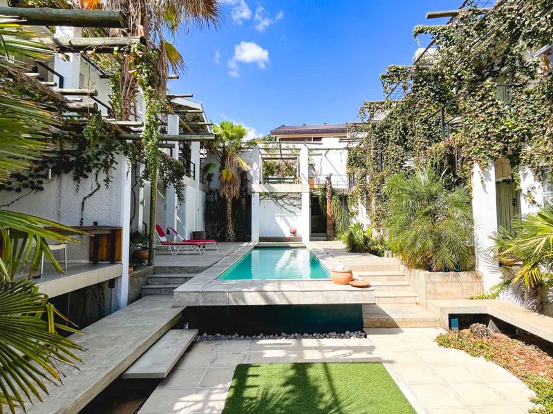 A central swimming pool area featuring a tiled pool surround, concrete steps, and pergola structures, surrounded by lush climbing vegetation and architectural retaining walls.