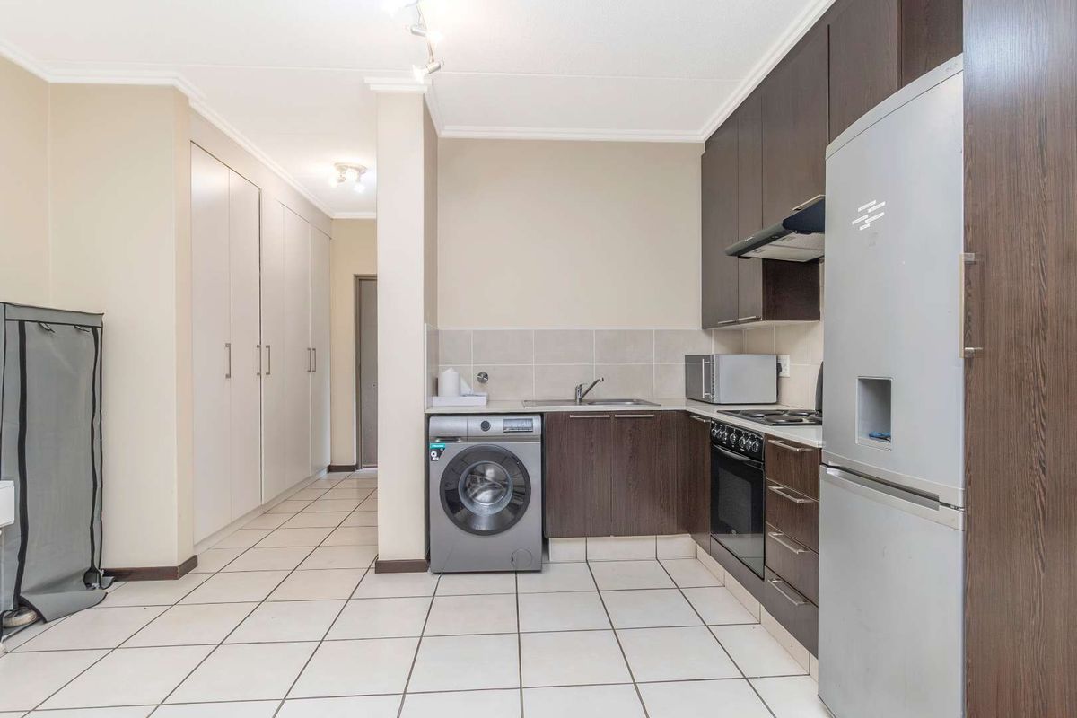 Compact kitchen featuring dark wood cabinetry, tiled backsplash, built-in oven with hob, extractor fan, and integrated laundry plumbing.
