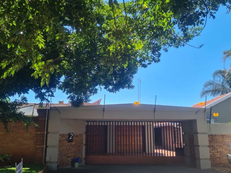 Front exterior view of the property featuring a paved driveway, secure sliding gate, and brick boundary wall with electric fencing.