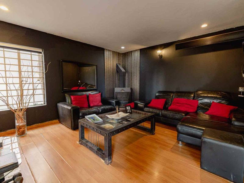 A living room featuring dark walls, wood flooring, and a corner fireplace with metal accent cladding.