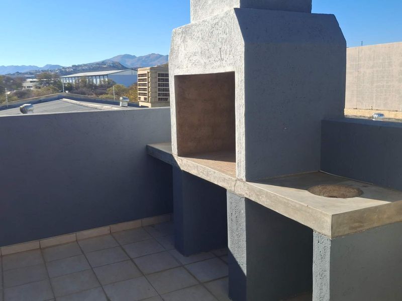 An outdoor balcony area featuring a built-in concrete braai and countertop, offering elevated views of the surrounding industrial landscape.