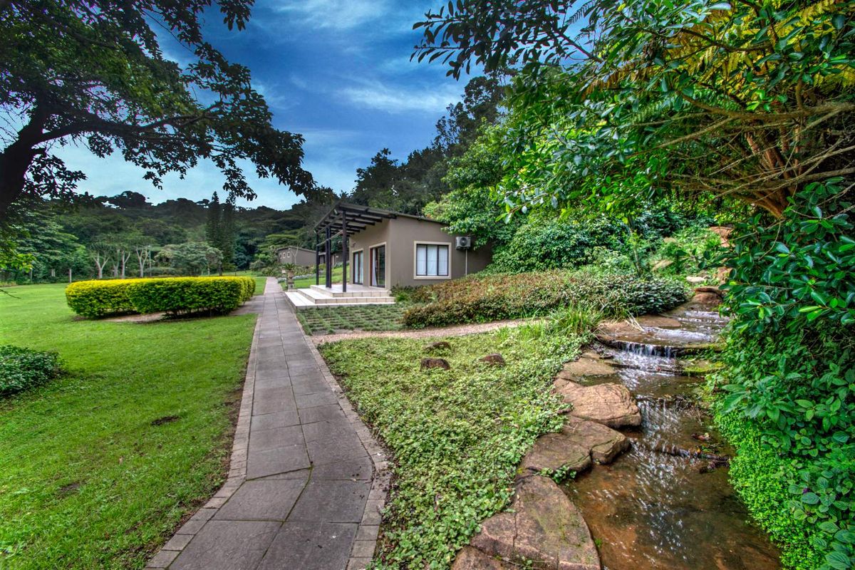 A scenic view of a guest house unit featuring a paved walkway, landscaped garden, and a natural stone-lined stream.