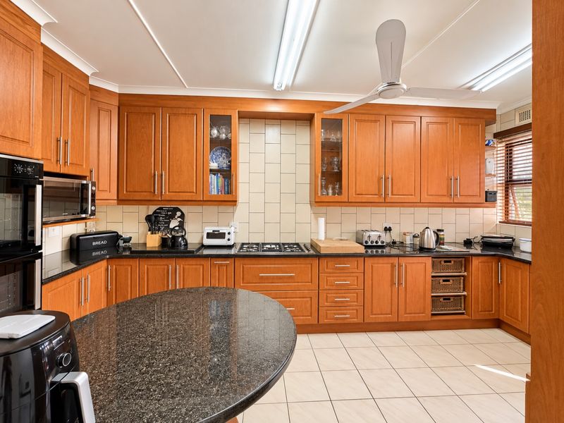 A functional kitchen featuring timber cabinetry, granite countertops, a gas cooktop, built-in oven, and tiled flooring, offering a classic and practical workspace.