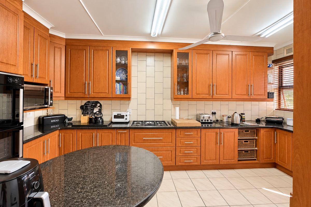 A functional kitchen featuring timber cabinetry, granite countertops, a gas cooktop, built-in oven, and tiled flooring, offering a classic and practical workspace.