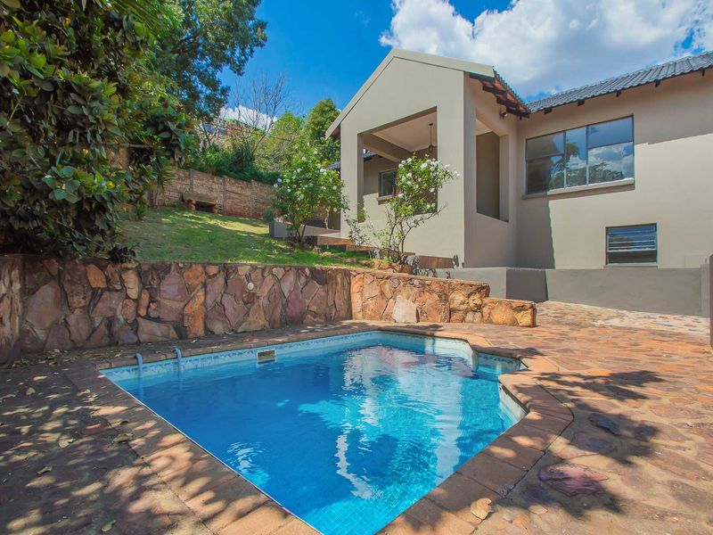 Outdoor pool area featuring a swimming pool, natural stone retaining wall, and flagstone paving, adjacent to a covered patio and the main house structure.