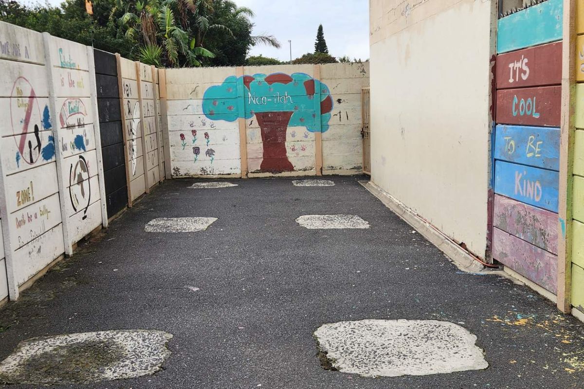 An outdoor rear courtyard area featuring precast concrete boundary walls with decorative murals and an asphalt paved surface.