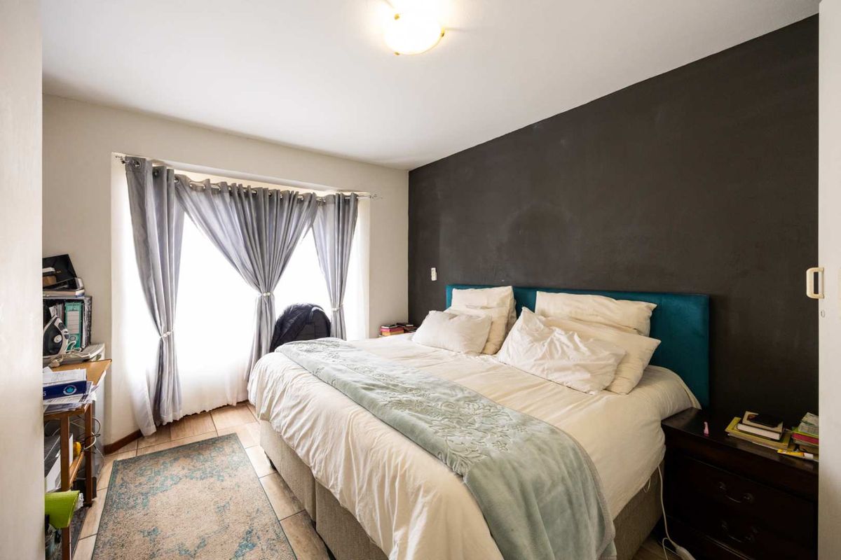 A bedroom featuring tiled flooring and a dark accent wall, providing a functional space with natural light from the window.