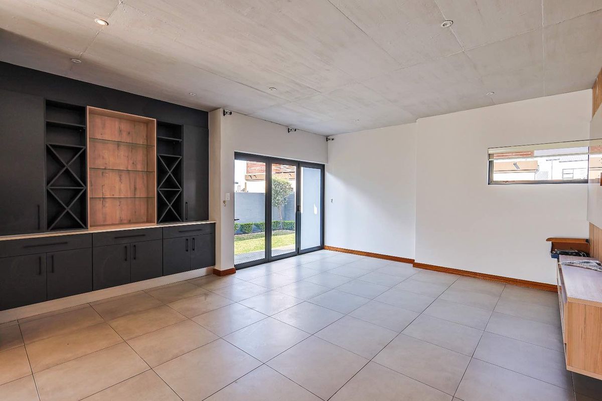Spacious living area featuring modern built-in cabinetry, tiled flooring, exposed concrete ceiling, and large sliding glass doors opening to the garden.