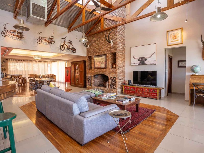 Spacious open-plan living area featuring a high vaulted timber-truss ceiling, exposed brick fireplace, and a combination of tiled and polished timber flooring.