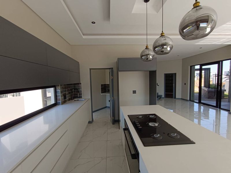 Modern kitchen featuring a central island with a built-in gas hob, sleek cabinetry, stone countertops, and high-end pendant lighting in an open-plan layout.
