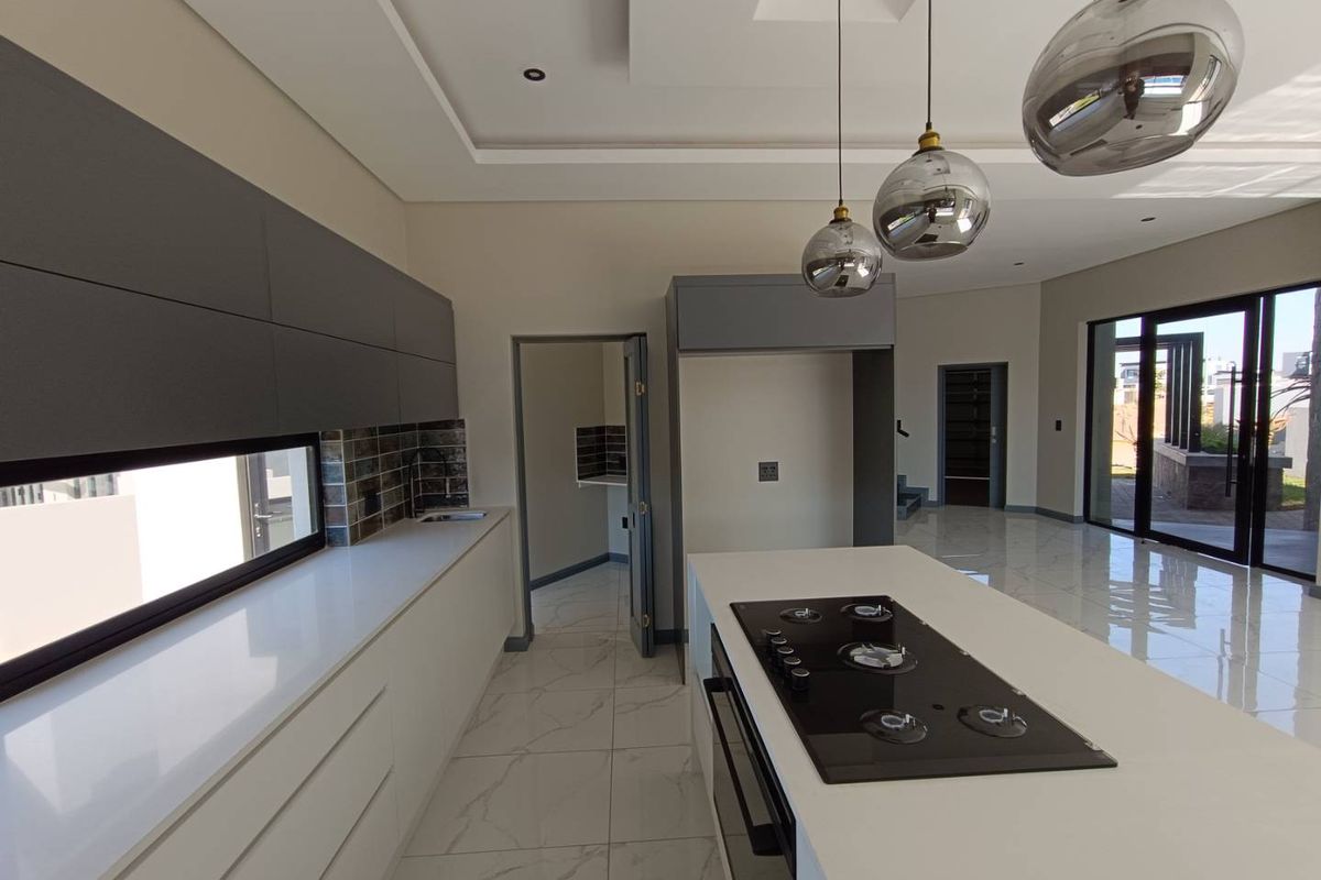 Modern kitchen featuring a central island with a built-in gas hob, sleek cabinetry, stone countertops, and high-end pendant lighting in an open-plan layout.