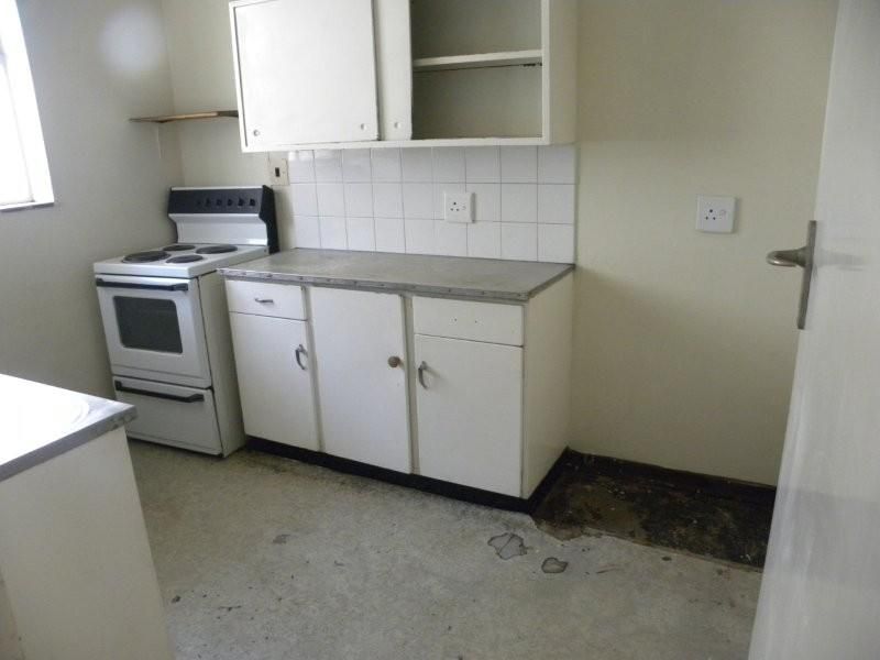 A dated kitchen featuring basic cabinetry, an electric stove, and tiled backsplash, requiring significant renovation and flooring repairs.
