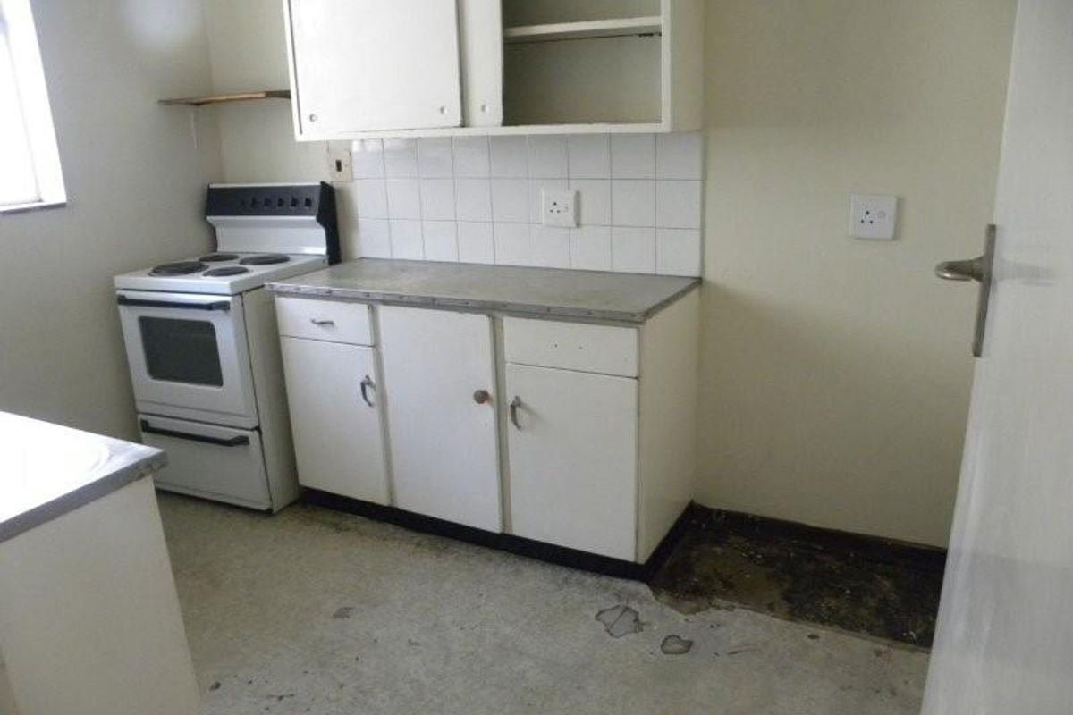 A dated kitchen featuring basic cabinetry, an electric stove, and tiled backsplash, requiring significant renovation and flooring repairs.