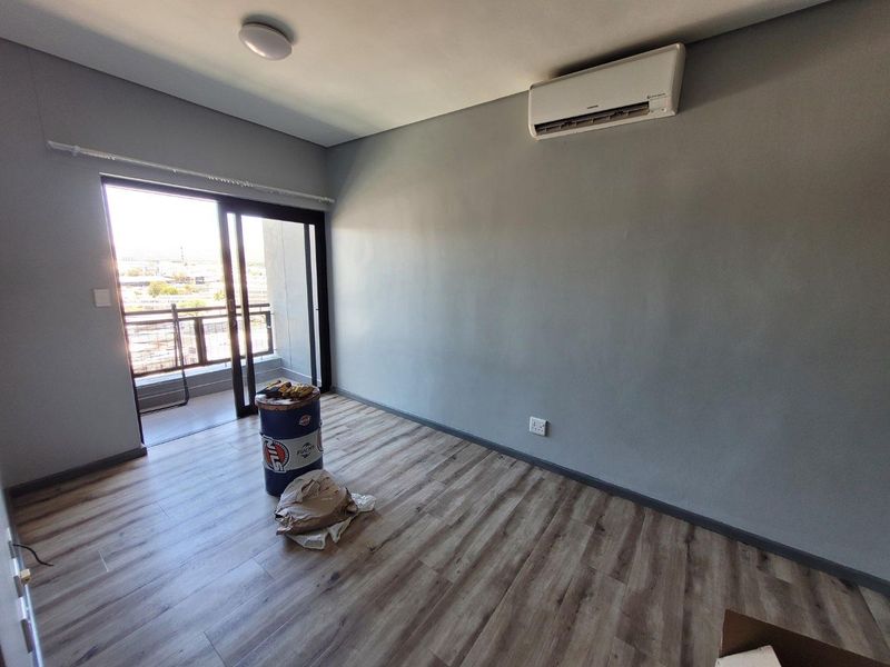 A bright, empty bedroom featuring modern laminate flooring, a wall-mounted split-system air conditioner, and a sliding glass door leading to a private balcony.