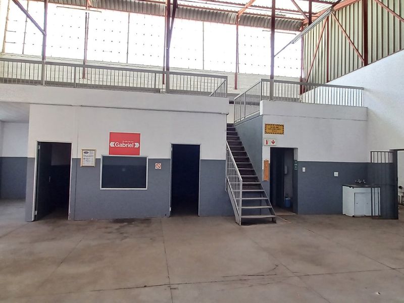 Spacious industrial warehouse featuring a mezzanine level with metal railings, concrete flooring, and multiple access points for versatile operational use.