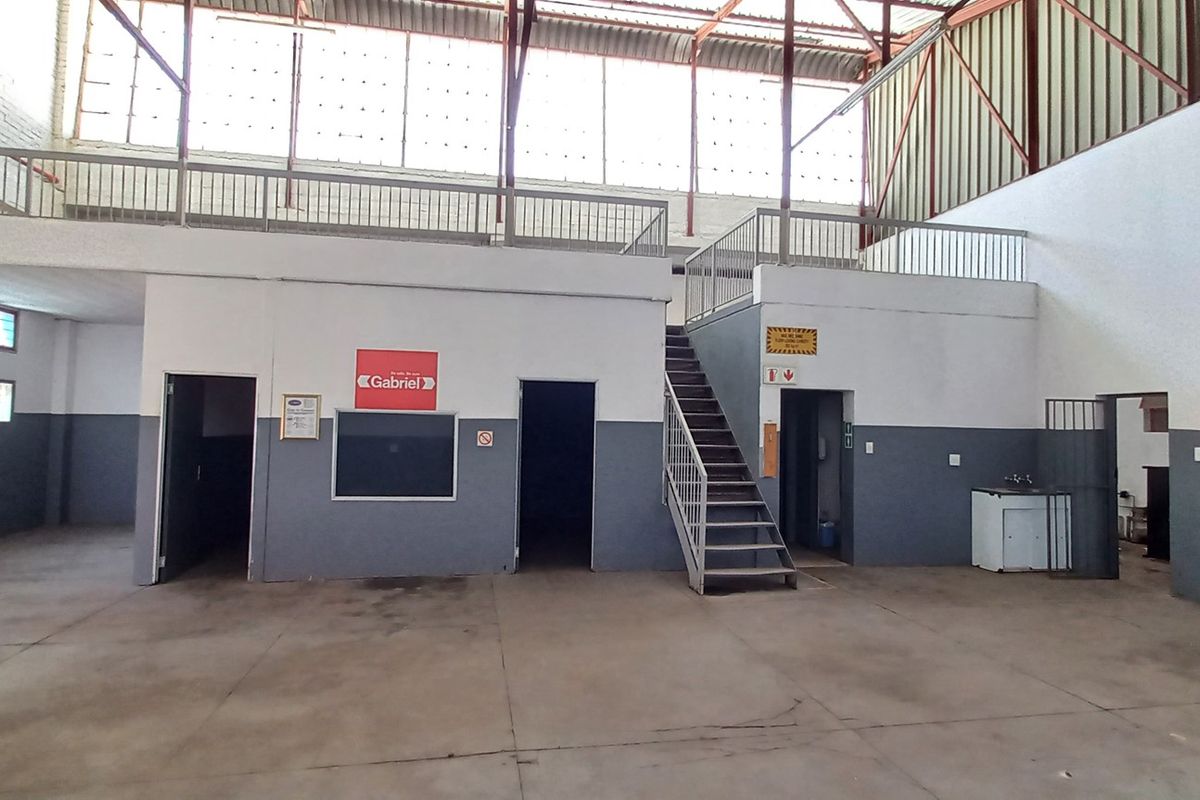 Spacious industrial warehouse featuring a mezzanine level with metal railings, concrete flooring, and multiple access points for versatile operational use.