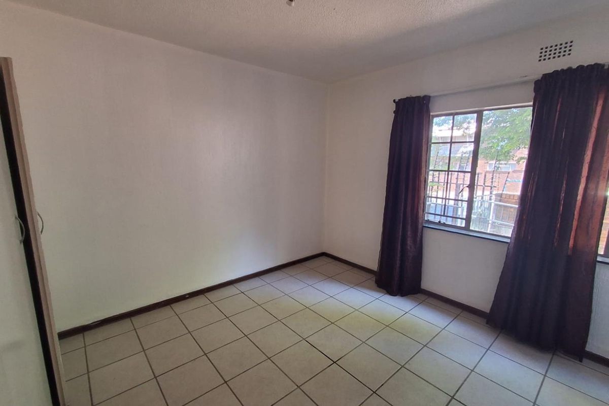 A simple bedroom featuring tiled flooring, a built-in cupboard, and a window with security bars.