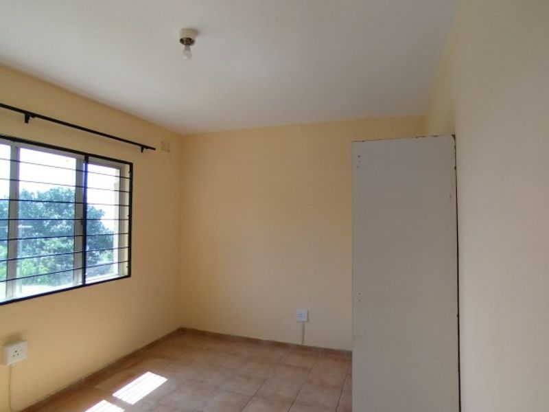 A vacant bedroom featuring tiled flooring, security bars on the window, and neutral wall paint, offering a blank canvas for potential updates.