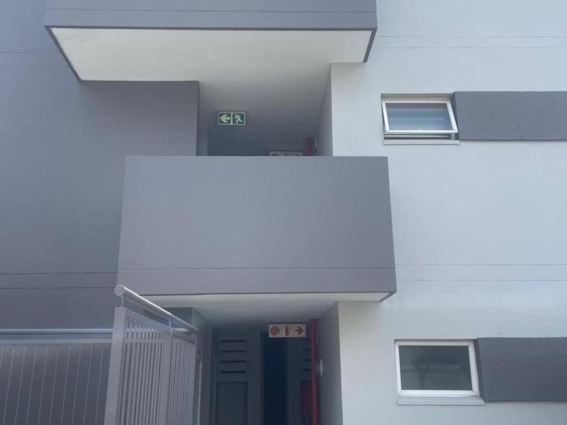 Exterior view of a modern apartment building entrance featuring grey facade, balconies, and clear signage for units 10-15.