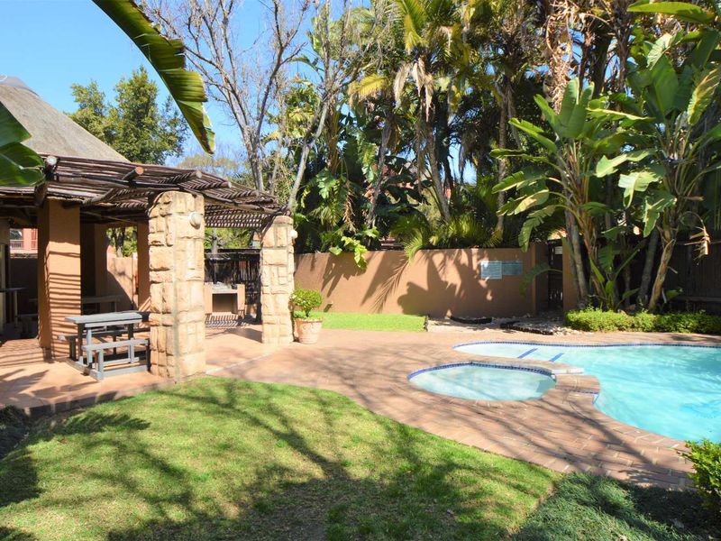 Outdoor entertainment area featuring a swimming pool, paved patio, and a thatched lapa with a built-in braai, surrounded by established garden landscaping.