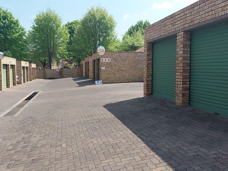 A view of a cluster complex driveway featuring multiple brick-built garages with green roller shutter doors and paved access areas.