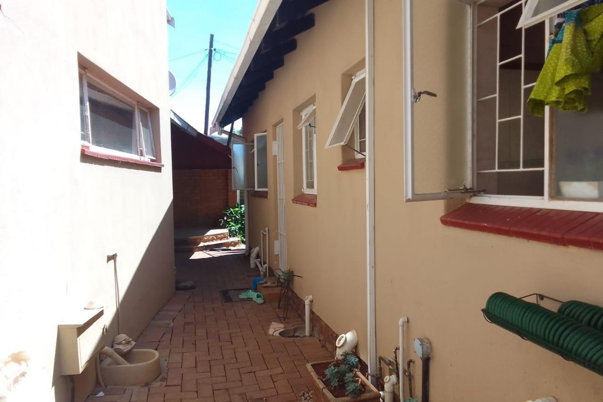 A side passage or rear exterior area featuring brick paving, security-fitted windows, and exposed roof rafters along the side of the house.