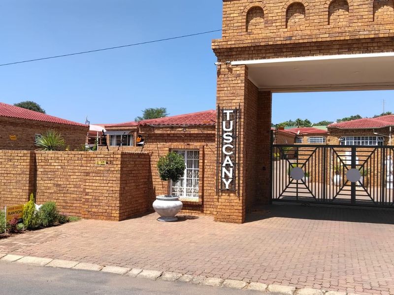 Front entrance view of the Tuscany townhouse complex featuring a brick facade, secure gated access, and a paved driveway.