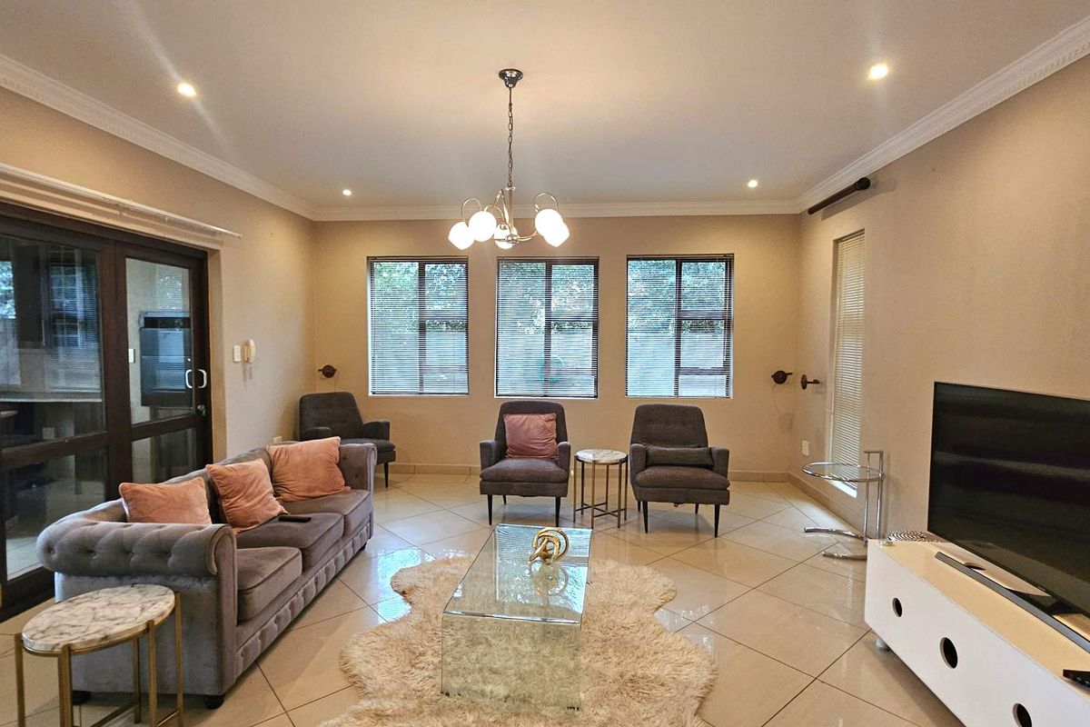 Spacious living room featuring neutral tiled flooring, recessed downlighting, crown molding, and large windows providing ample natural light.