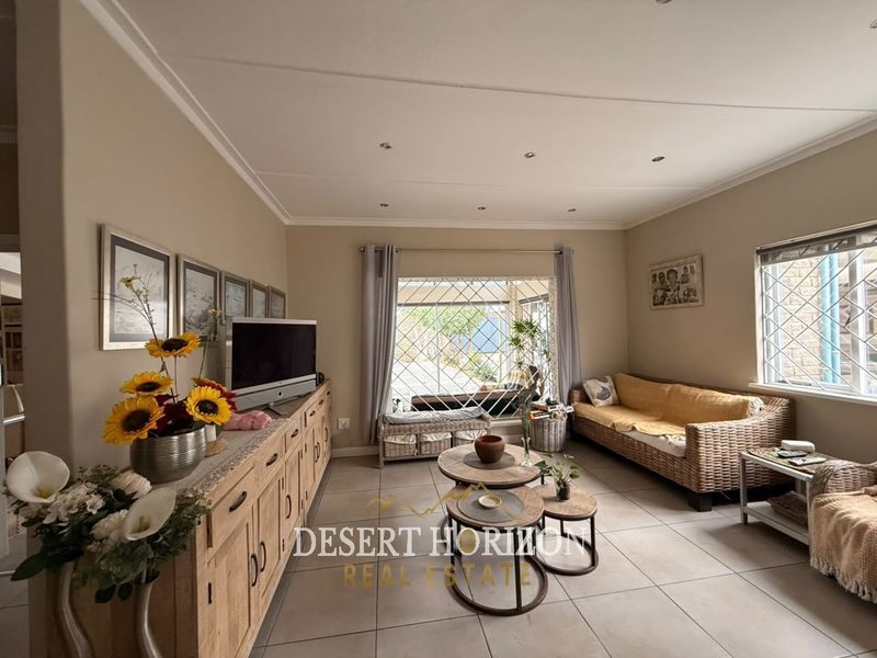 A comfortable living room featuring tiled flooring, recessed ceiling lighting, and large windows fitted with security bars, providing a bright and functional living space.