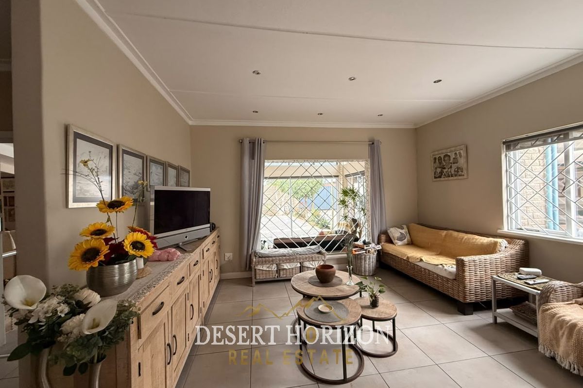 A comfortable living room featuring tiled flooring, recessed ceiling lighting, and large windows fitted with security bars, providing a bright and functional living space.