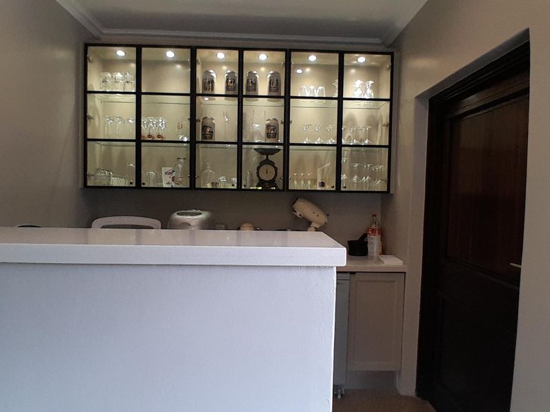A well-maintained home bar area featuring a solid counter and illuminated glass-fronted display cabinetry for glassware storage.