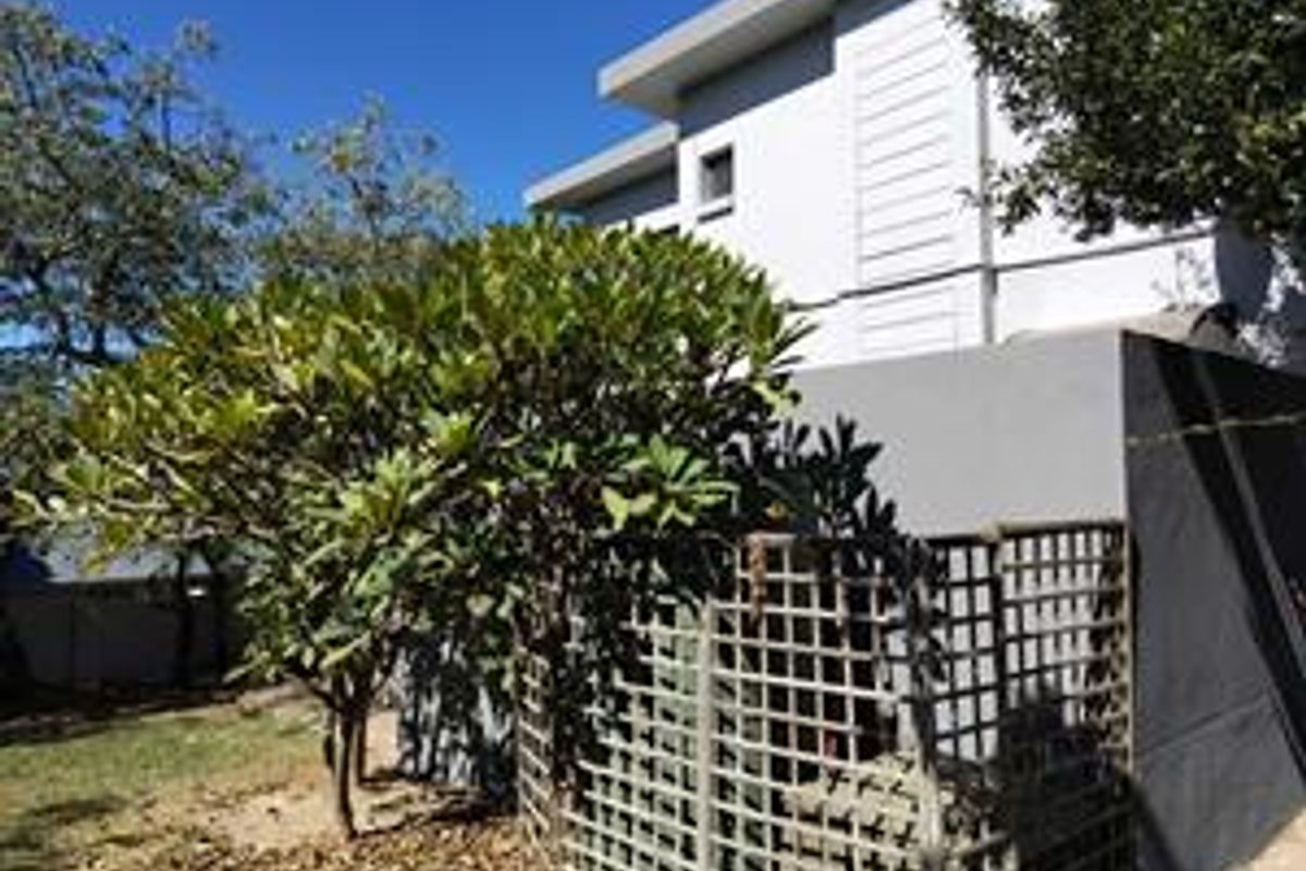 Rear view of the property showing a modern building facade, a concrete boundary wall, and a lattice screen enclosure.
