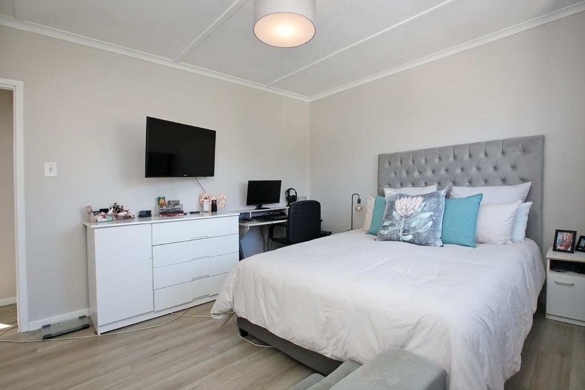 A well-maintained bedroom featuring light-toned laminate flooring, neutral wall finishes, and a coved ceiling with a central pendant light.