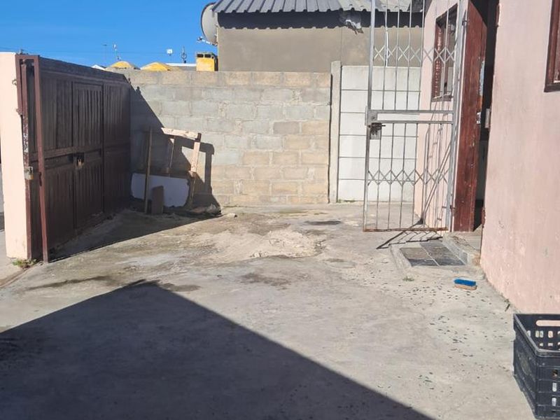 A rear exterior area featuring a concrete driveway, security gate, and boundary wall, showing signs of wear and requiring maintenance.