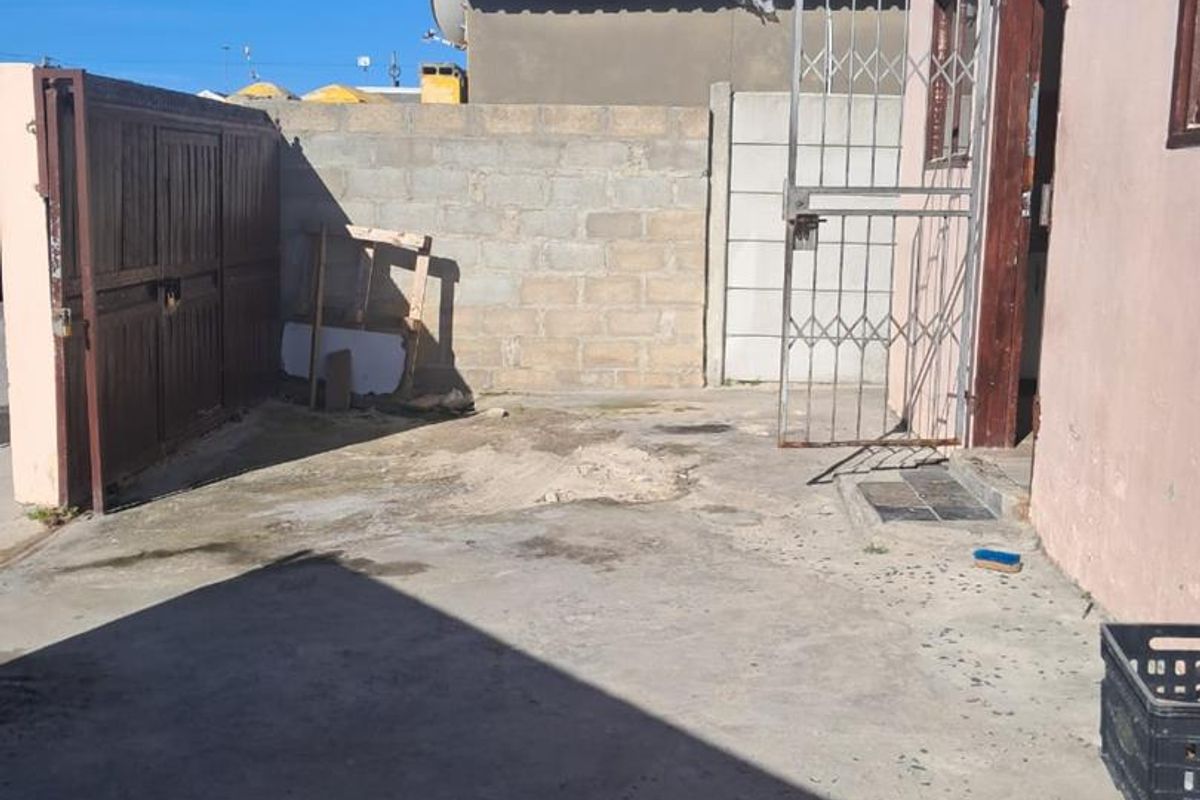 A rear exterior area featuring a concrete driveway, security gate, and boundary wall, showing signs of wear and requiring maintenance.