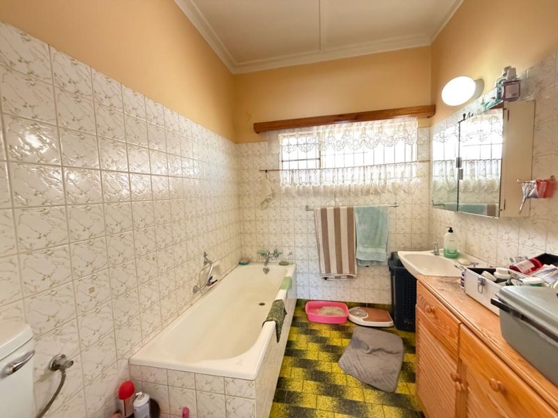 A dated bathroom featuring a built-in vanity, ceramic washbasin, and a bathtub with wall-mounted taps, finished with traditional wall tiling.