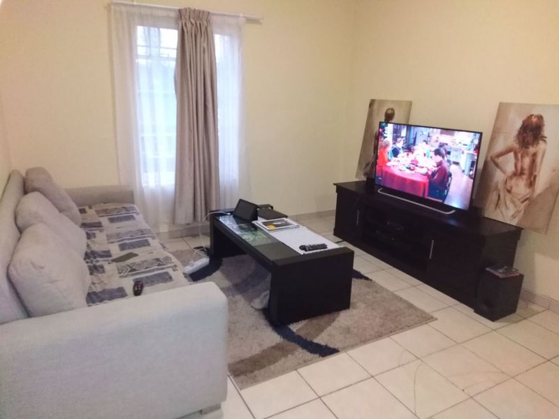 A standard living room featuring tiled flooring and a window with curtain fixtures, providing a functional and neutral space for relaxation.