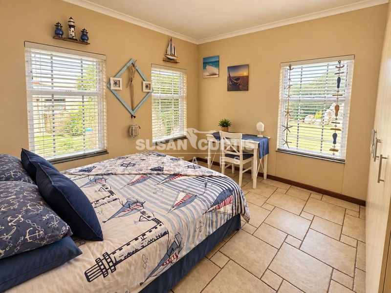 A bright bedroom featuring tiled flooring, built-in wardrobe storage, and multiple windows with venetian blinds overlooking the garden.