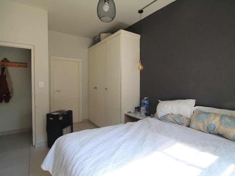 A bedroom featuring tiled flooring, a built-in wardrobe, and a dark accent wall, providing a functional space with neutral finishes.