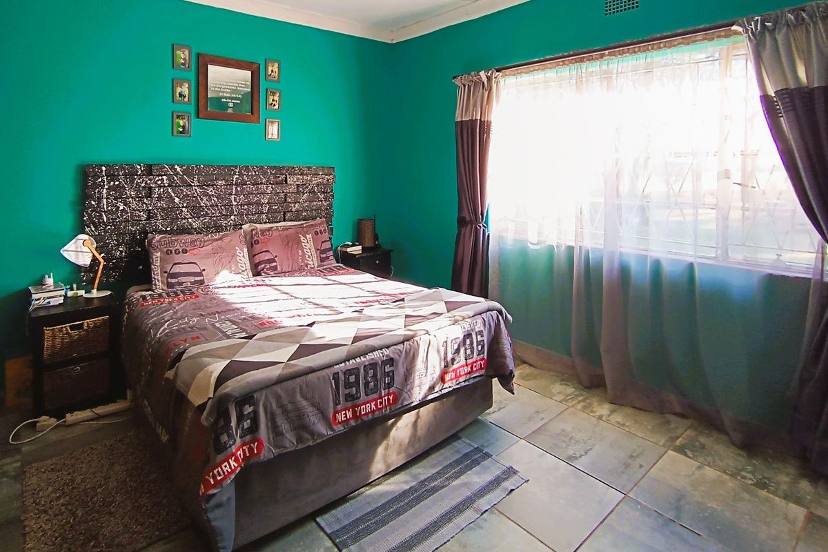 A bedroom featuring tiled flooring and a large window allowing natural light, providing a functional space for rest.