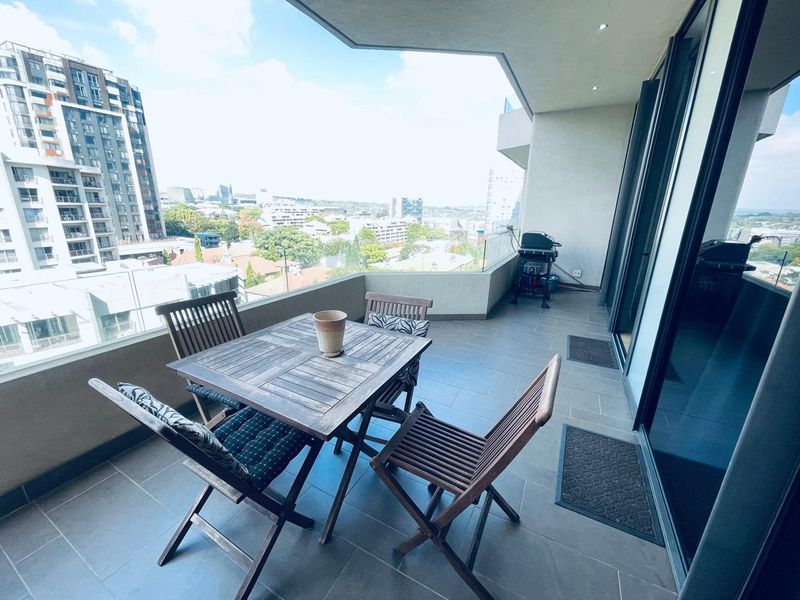 Spacious covered balcony featuring tiled flooring, a glass balustrade, and recessed lighting, offering expansive urban views.