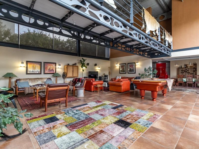 Spacious open-plan living area featuring high vaulted ceilings, an industrial-style exposed steel mezzanine walkway, and large format floor tiles.