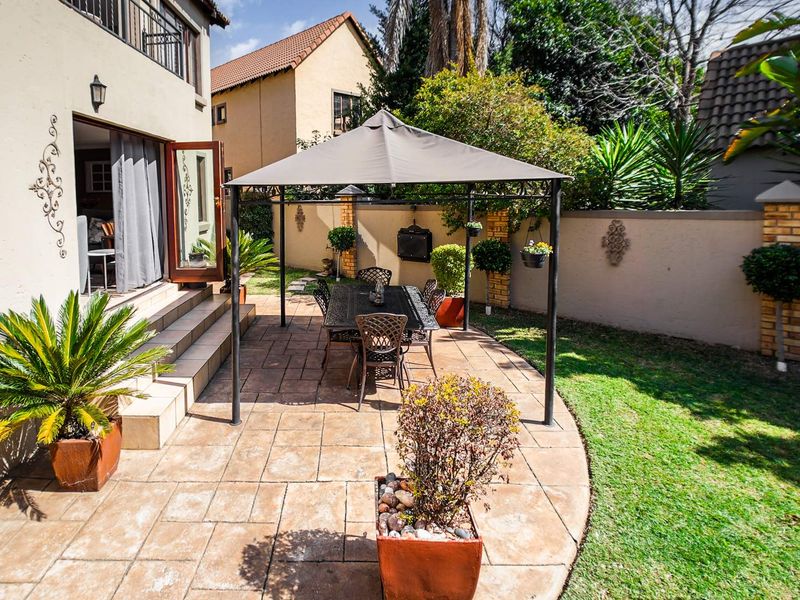 A private rear garden featuring a paved patio area, built-in braai, and direct access to the townhouse interior via double doors.